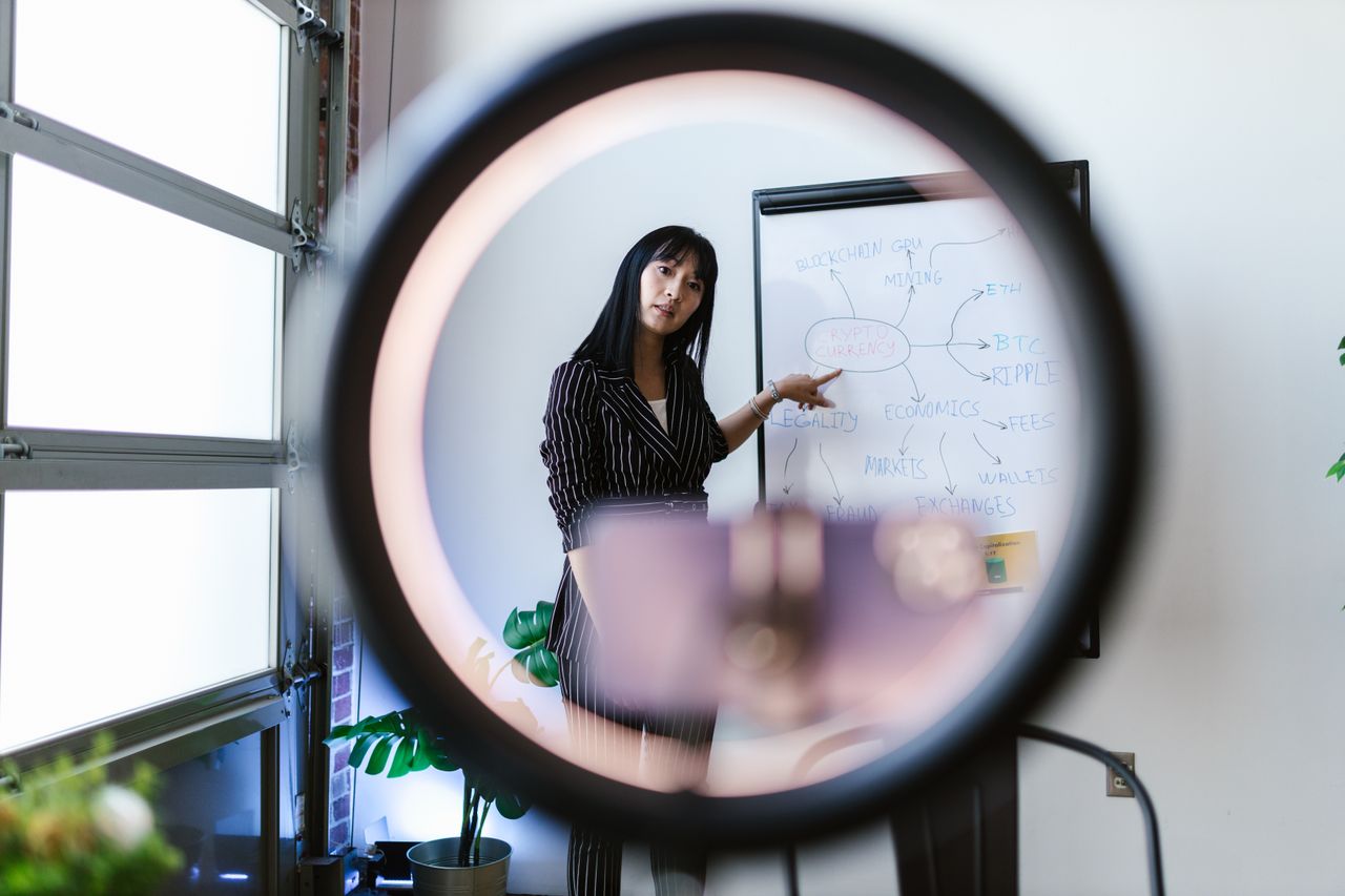 A woman uses a ring light for an online presentation on economics and cryptocurrency.
